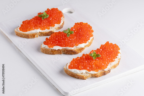 Three sandwiches with red caviar on a cutting board. A delicious appetizer of trout caviar on a slice of bread with cream cheese. Salted salmon caviar for fish delicacy concept