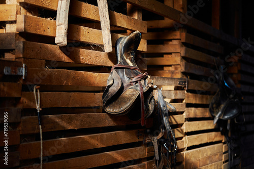 The brown saddle on the wooden stable door is a close-up. Worn saddle for horses made of genuine leather.