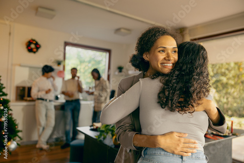 Happy young female friends hugging and enjoying time together at holiday party at home