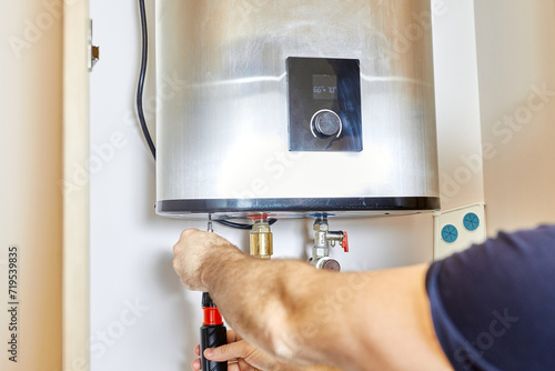 the man tightens the pipe nut in the water heating system. The master installs the water heater. The concept of bathroom maintenance. photo