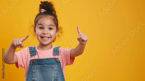 young girl with a joyful expression, pointing both of her fingers to her sides against a bright yellow background
