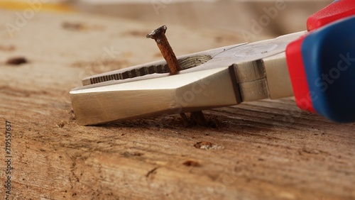 Close-up of Pliers Pulling a Rusty Nail out of an old Wooden Board.