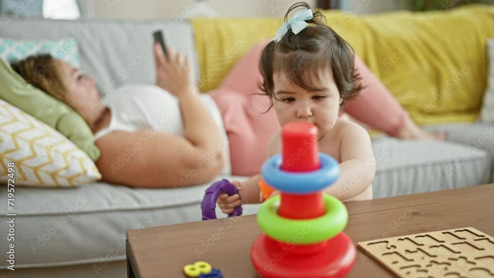 Mother and daughter lying on the sofa at home, sharing love and laughter while playing a hoops game on their smartphone Mother and daughter lying on the sofa at home, sharing love and laughter while playing a hoops game on their smartphone