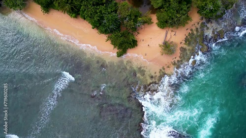 Slow cinematic backwards flight from jungle coast line over waves of blue ocean photo