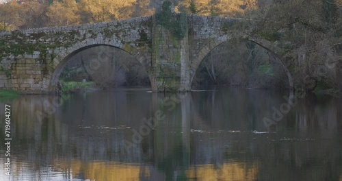 Medieval stone roman bridge over Arnoia river in Allariz with blurred people crossing in Galicia Spain photo