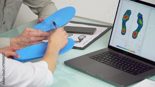 Doctor consulting male patient on custom orthotic insoles in a clinic for a personalised custom fitusing test picture on a laptop.