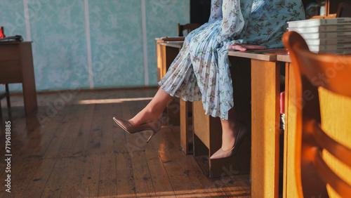 A young girl sits on a table with her legs overhanging her shoes.