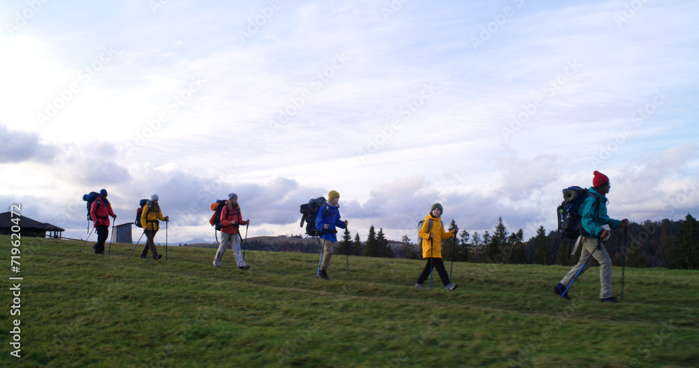 Full shot of diverse group of tourists walking on trail after sleepover in big house. Hiking buddies during trip or trek to mountains on their vacation in autumn. Tourism and active leisure concept. Full shot of diverse group of tourists walking on trail after sleepover in big house. Hiking buddies during trip or trek to mountains on their vacation in autumn. Tourism and active leisure concept.