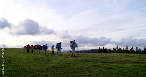 Full shot of diverse group of tourists walking on trail after sleepover in big house. Hiking buddies during trip or trek to mountains on their vacation in autumn. Tourism and active leisure concept.