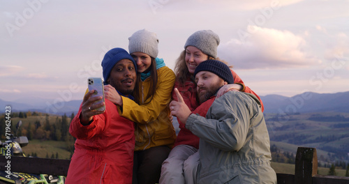 Hiking buddies stand near wooden fence and look at sunset. Group of diverse tourists or travelers enjoy the mountains landscape and beautiful nature during trip. Outdoor enthusiasts. Slow motion.