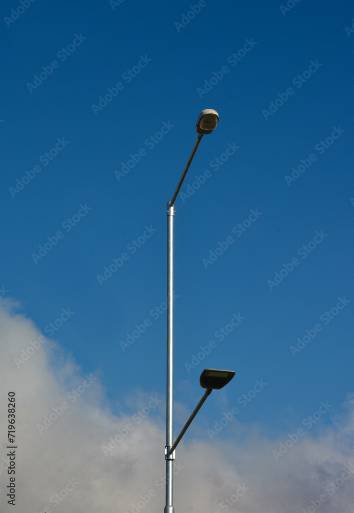 Postlamp with two symmetrical lamps in a city on a blue sky with clouds in the bottom. Symmetrical urban photography. Atmospheric image. Postlamp with two symmetrical lamps in a city on a blue sky with clouds in the bottom. Symmetrical urban photography. Atmospheric image.