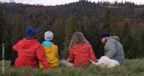 Obraz na plátně Diverse tourists or hiking buddies sit on the grass at the hilltop and pet dog