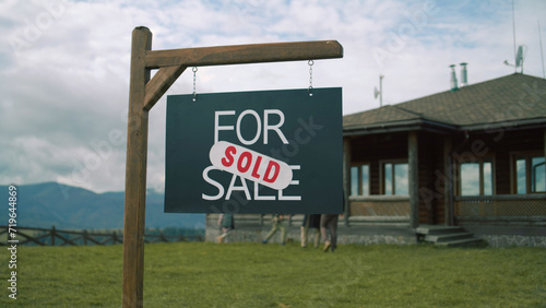 For sale sign on beautiful green lawn. African American real estate agent comes and puts sold sticker on sign. Modern cottage with traditional architecture in mountains. Residential property on sale.