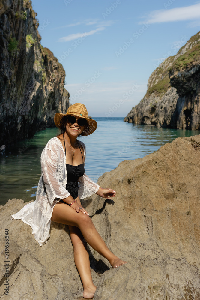 Beautiful young Latin woman, poses on a paradisiacal beach, wearing a white blouse and a straw hat