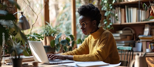 Smiling young black woman sitting at desk working on laptop taking notes in notebook happy millennial female study watching webinar using computer writing check list banner panorama free copy s photo