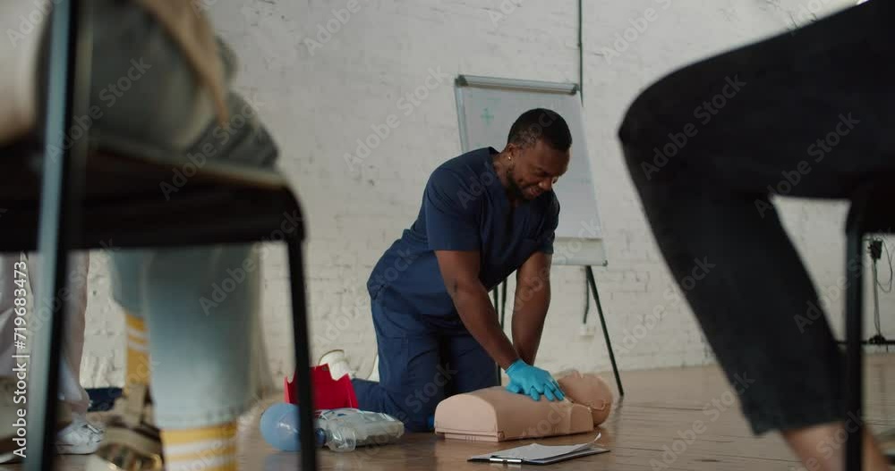 Bottom view: A Black male doctor in blue uniform conducts a practice session showing artificial respiration on a medical mannequin Bottom view: A Black male doctor in blue uniform conducts a practice session showing artificial respiration on a medical mannequin