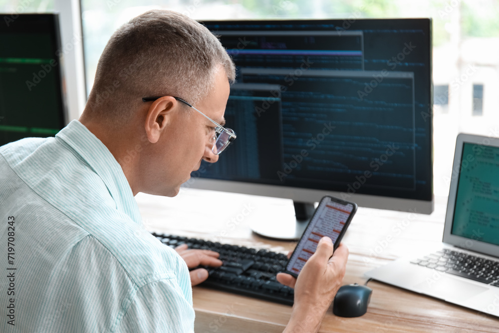 Mature male programmer with mobile phone working in light office