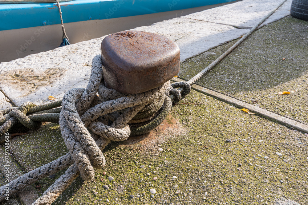 Fototapeta premium Close-up of a knot made with a fishing boat rope moored to an iron peg in a port in Grado, Italy. Articles for fishing boats. Marine items.