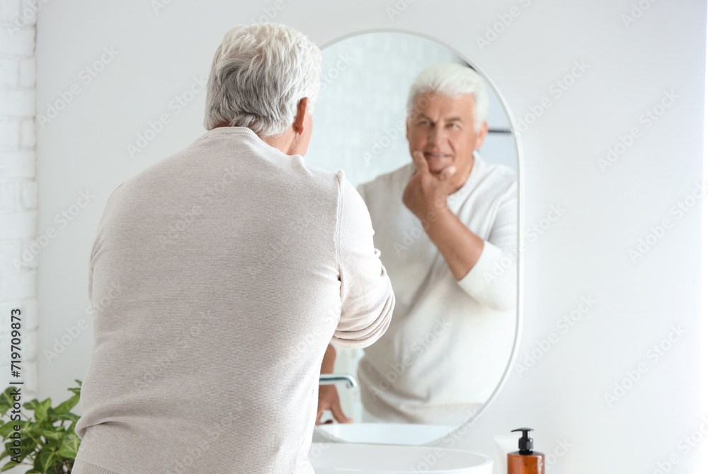 Fototapeta premium Senior man looking in mirror at home, back view
