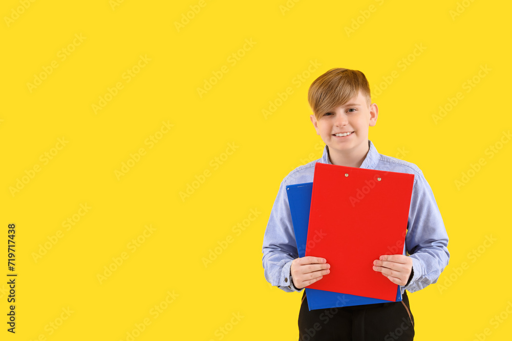 Little schoolboy in stylish uniform with notebooks on yellow background Little schoolboy in stylish uniform with notebooks on yellow background