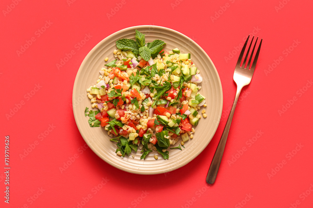 Plate with delicious tabbouleh salad and fork on red background Plate with delicious tabbouleh salad and fork on red background