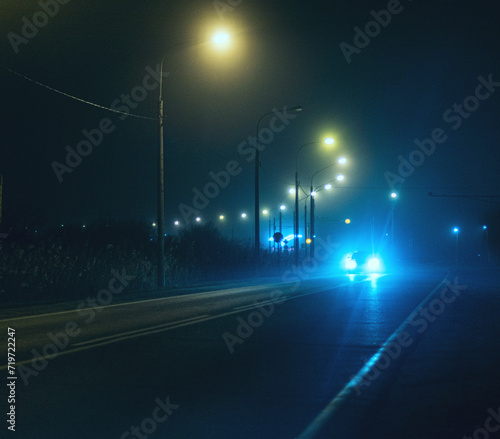 Tableau sur toile The headlights of an oncoming car tear through the darkness of the city at night