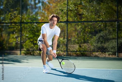 A young man hits a tennis ball on a tennis court © joescarnici