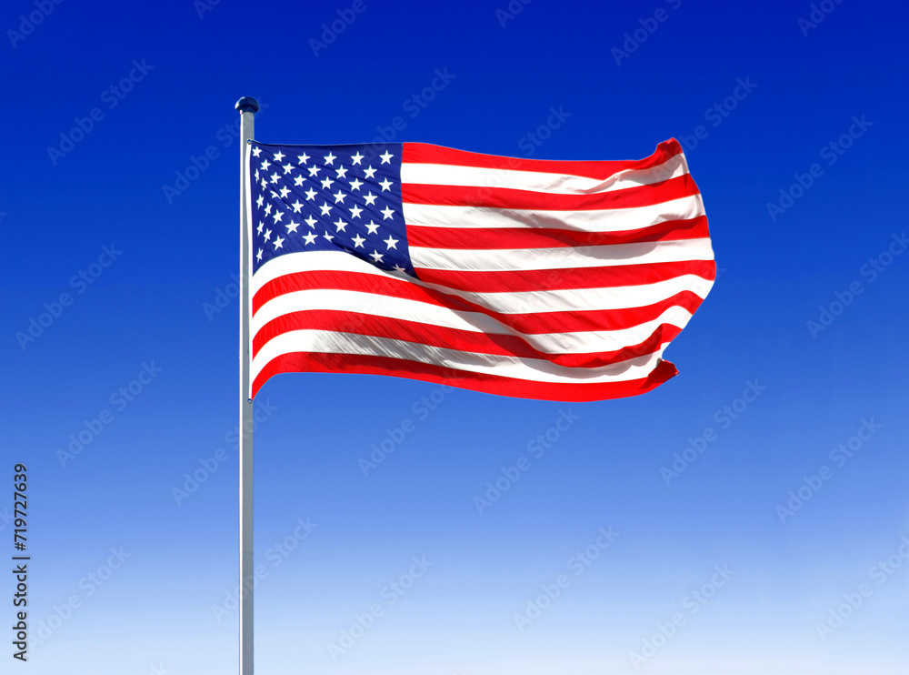 the national flag of the USA flies in the wind on a flagpole with a blue sky as a backdrop