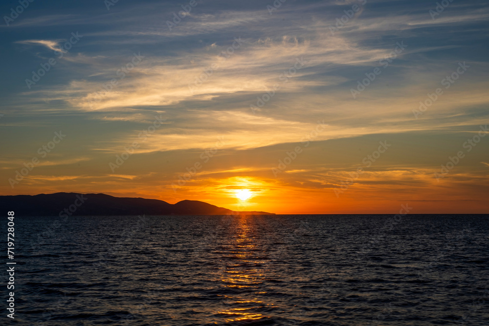 Sunset at Aegean sea at Zakynthos island in Greece. Sun setting behind the mountain