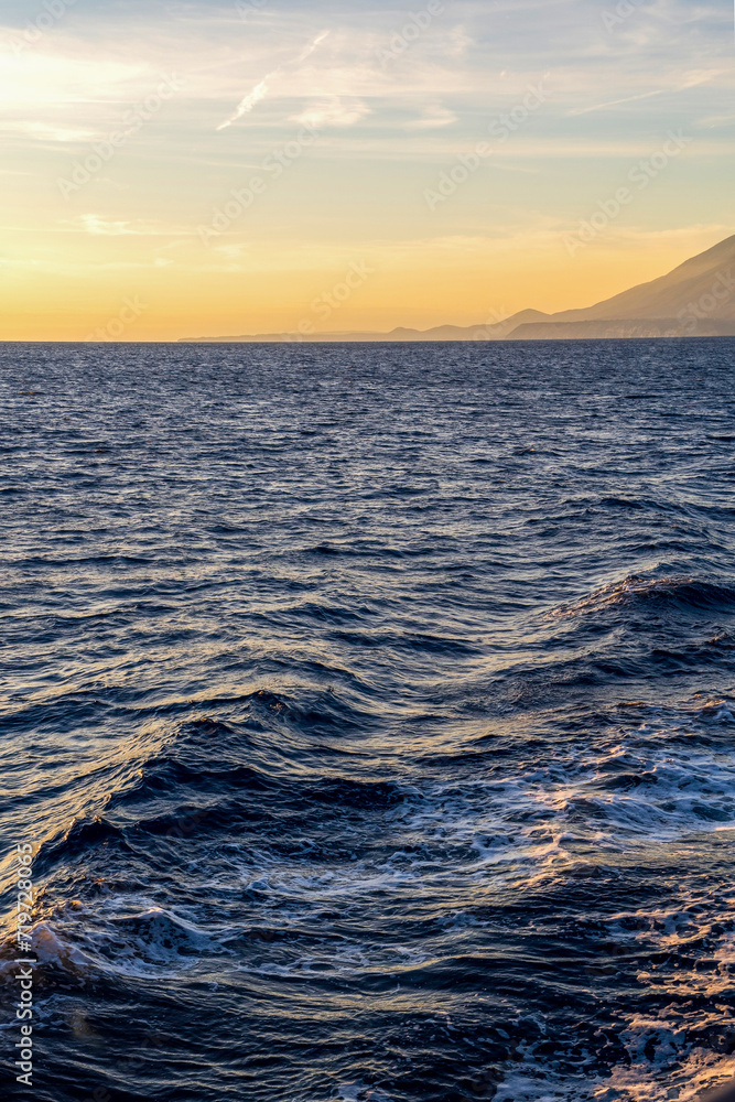 waves on a sea against golden sky and mountain on an island in Greece, Europe