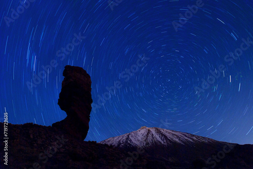 the Roque Cinchado at night with circling stars in the clear night sky and the summit of Pico de Teide, Tenerife, Canary Islands, Spain