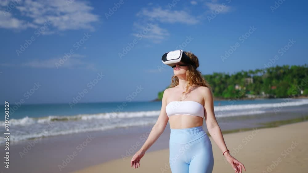 Woman in VR headset explores virtual realm on sunny beach. Interactive tech blends reality, gaming. User gestures in simulated environment. VR tourism, immersive experience in coastal setting. Slowmo Woman in VR headset explores virtual realm on sunny beach. Interactive tech blends reality, gaming. User gestures in simulated environment. VR tourism, immersive experience in coastal setting. Slowmo