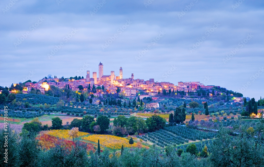 Town view of San Gimignano on a hill in the early morning at blue hour with cloudy sky in fall, all around are cypresses, olive groves and vineyards, Tuscany, Italy, Europe