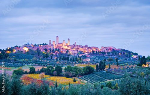 Town view of San Gimignano on a hill in the early morning at blue hour with cloudy sky in fall, all around are cypresses, olive groves and vineyards, Tuscany, Italy, Europe