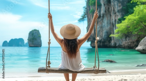 beautiful Asian woman ware a straw hat and sat on a swing made of wood, tied to a rope, facing the sea at a sunny time. © buraratn