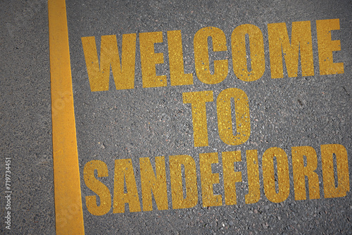 asphalt road with text welcome to Sandefjord near yellow line. photo