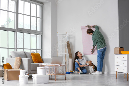 Young couple with Beagle dog wallpapering during repair in their new house photo