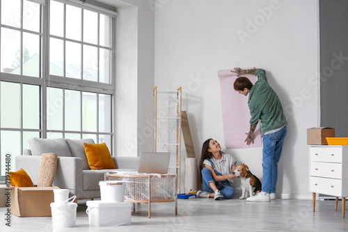 Young couple with Beagle dog wallpapering during repair in their new house