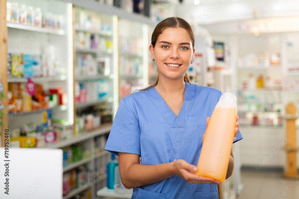 Female drugstore worker showing haircare product while standing in salesroom of drugstore