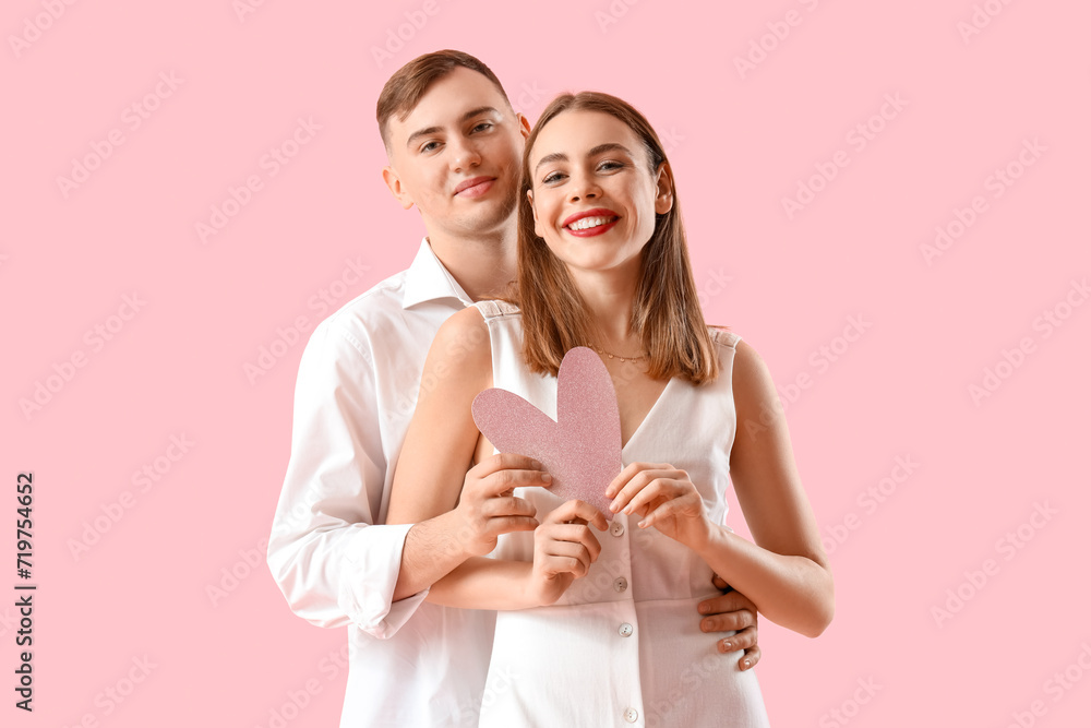 Happy young couple with paper heart on pink background. Valentine's Day celebration Happy young couple with paper heart on pink background. Valentine's Day celebration