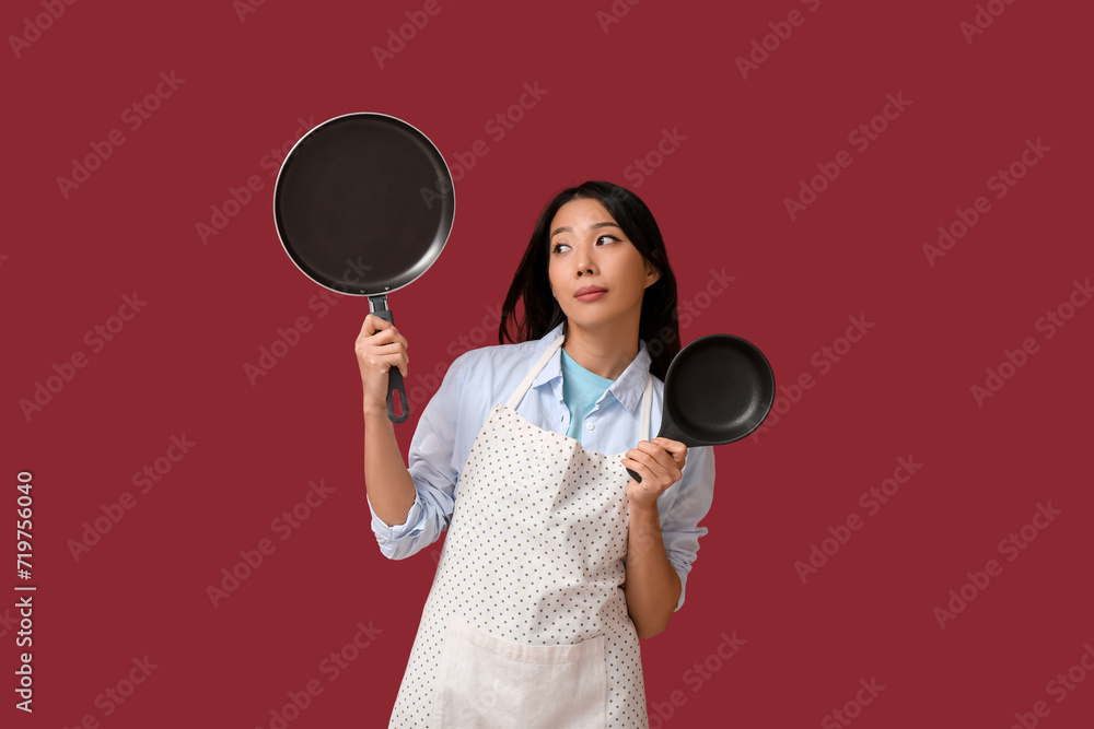 Portrait of young Asian woman with frying pans on red background Portrait of young Asian woman with frying pans on red background