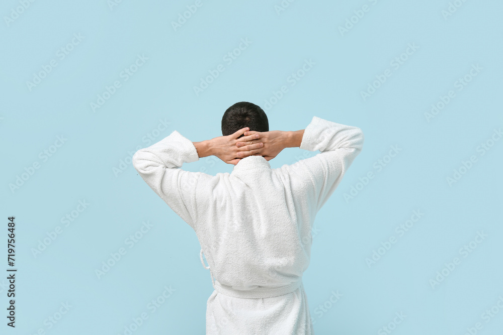 Handsome young man in bathrobe on blue background, back view Handsome young man in bathrobe on blue background, back view