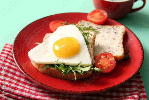Plate with tasty fried egg, toasts, tomatoes and arugula on turquoise background, closeup