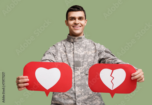Young happy male soldier with heart like and dislike icons on green background photo