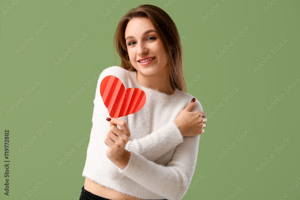 Beautiful young woman with red paper heart on green background. Valentine's Day celebration