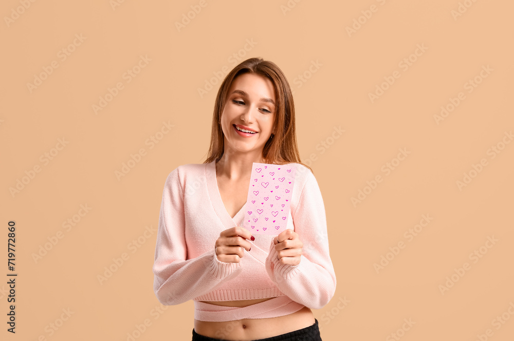 Happy young woman holding greeting card with hearts on beige background. Valentine's Day celebration Happy young woman holding greeting card with hearts on beige background. Valentine's Day celebration