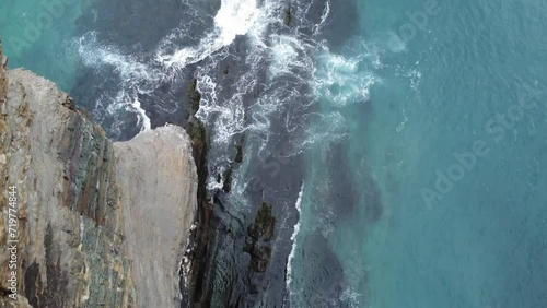 Drone shot going over the edge of a 300ft cliff with waves crashing against the coast below photo