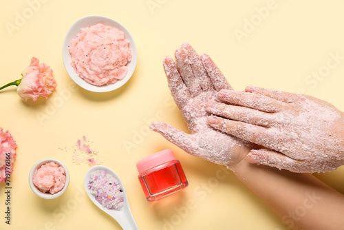 Photos Female hands with scrub, sea salt and cosmetic oil on light yellow background