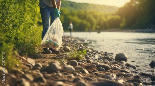 Closeup of a young volunteer holding a trash bag and picking up litter along a riverbank. photo