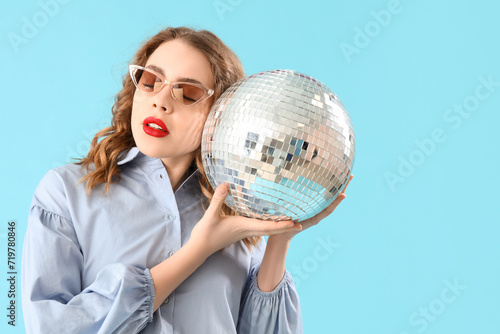 Beautiful young stylish woman with disco ball on blue background